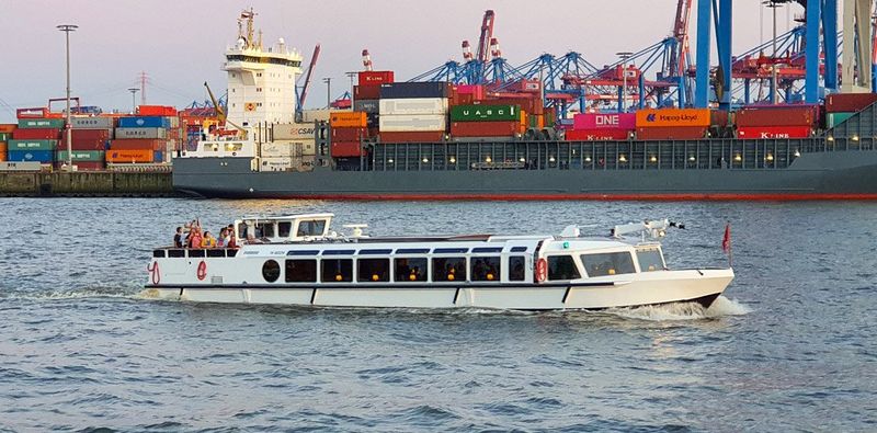 Weißes mittelgroßes Partyschiff vor dem Containerterminal im Hamburger Hafen